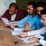 Group of four south asian men's posed at business meeting in cafe. Indians together and sign important documents. Contract to study and work.